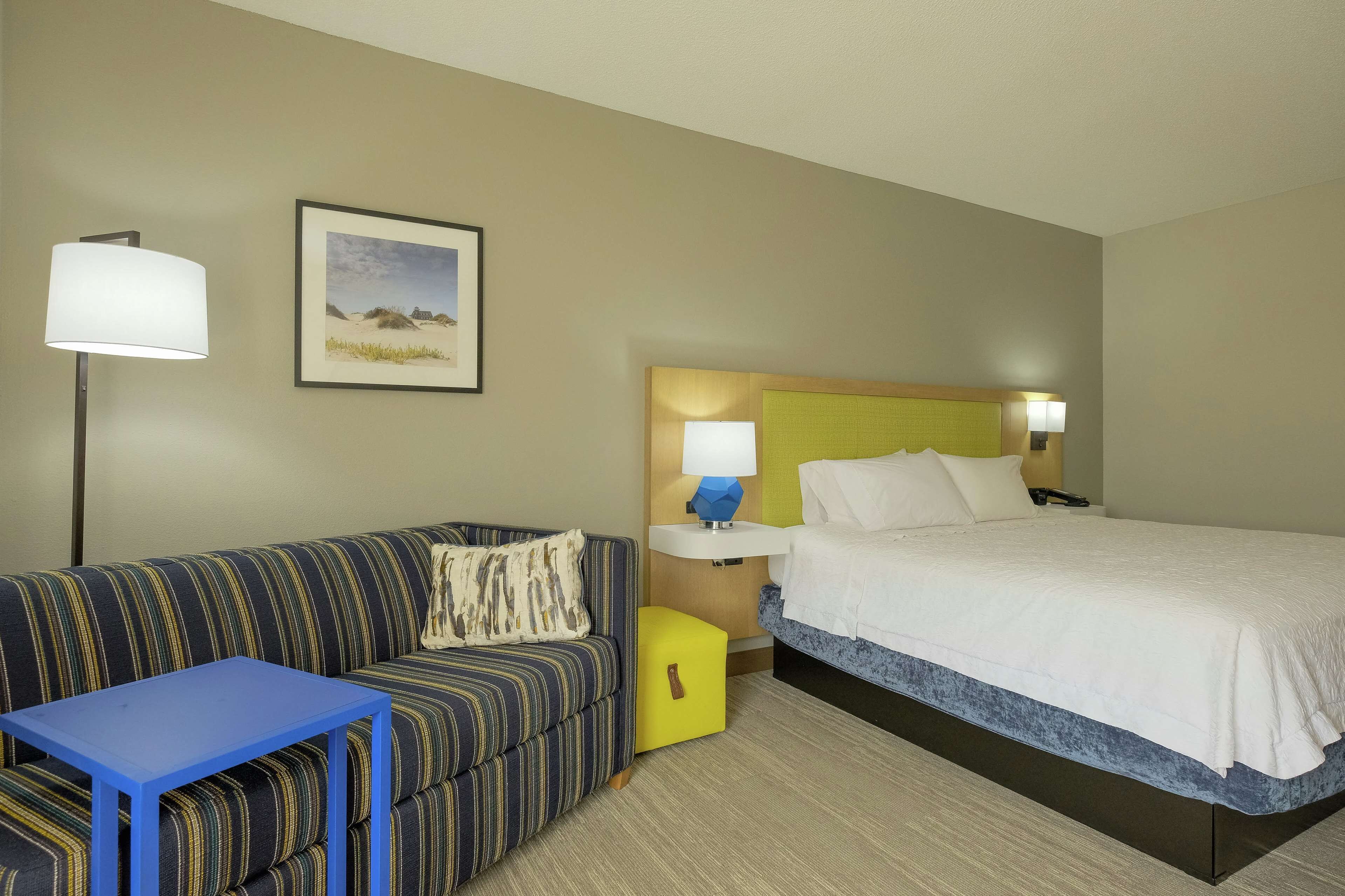 Une chambre d’hôtel avec un lit, un canapé, une petite table, une table de chevet et une lampe.