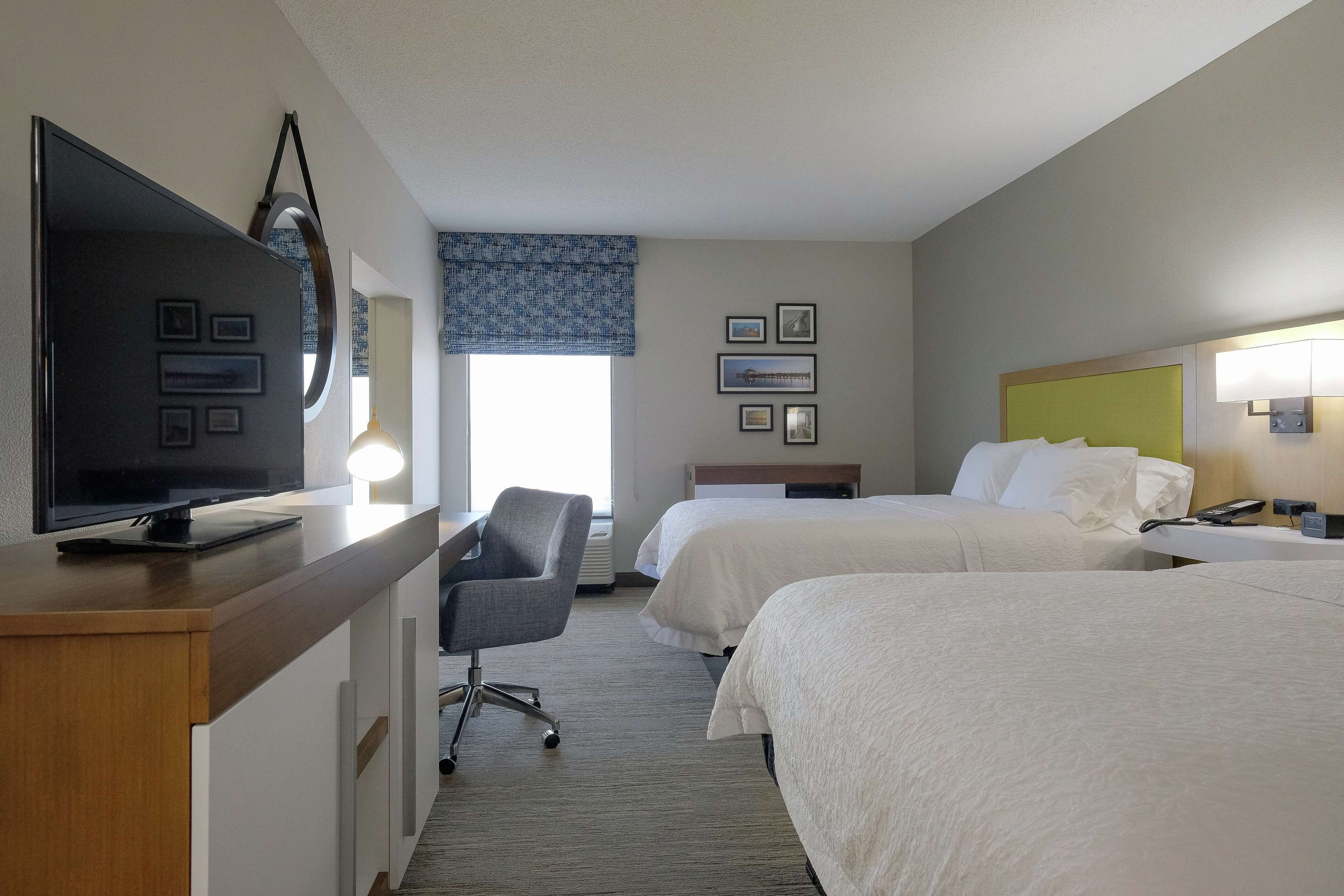 A hotel room with two beds, a TV, a desk, and a chair.