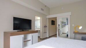 Ett hotellrum med en säng, en tv på ett träställ, ett skrivbord med en lampa och en spegel.
