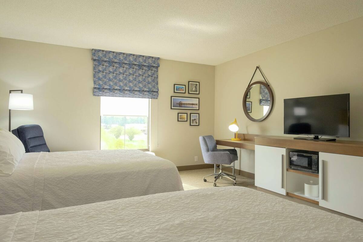 Habitación de hotel con dos camas, un escritorio con computadora, televisor y ventana con vistas.