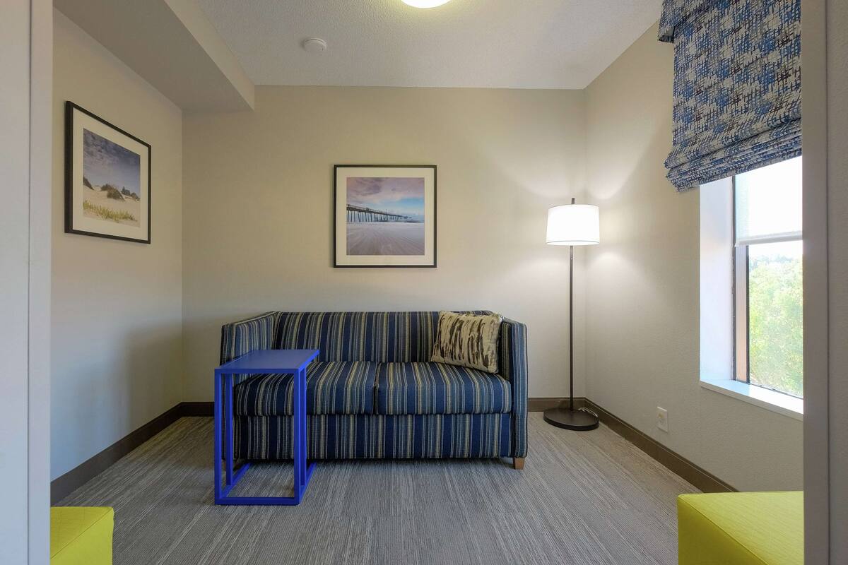 Una habitación con un sofá a rayas, una mesita, una lámpara y dos cuadros en la pared.