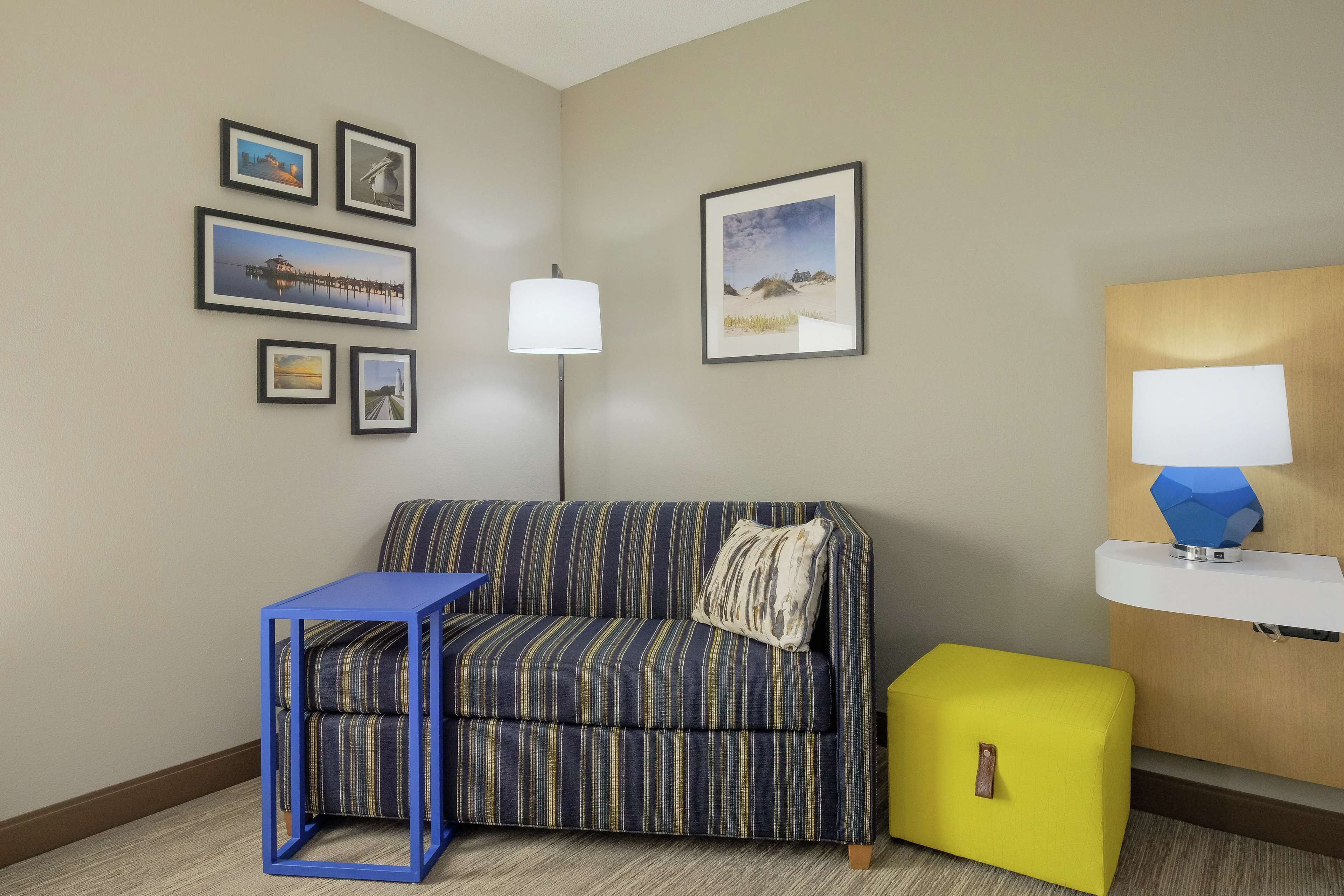 A room with a striped sofa, a small blue table, a yellow ottoman, and a wall with framed pictures.