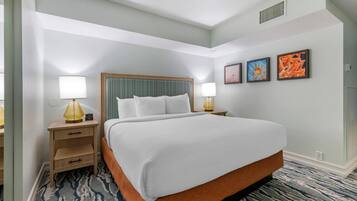 A hotel room with a large bed, two bedside tables with lamps, a small drawer unit, and three framed pictures on the wall.