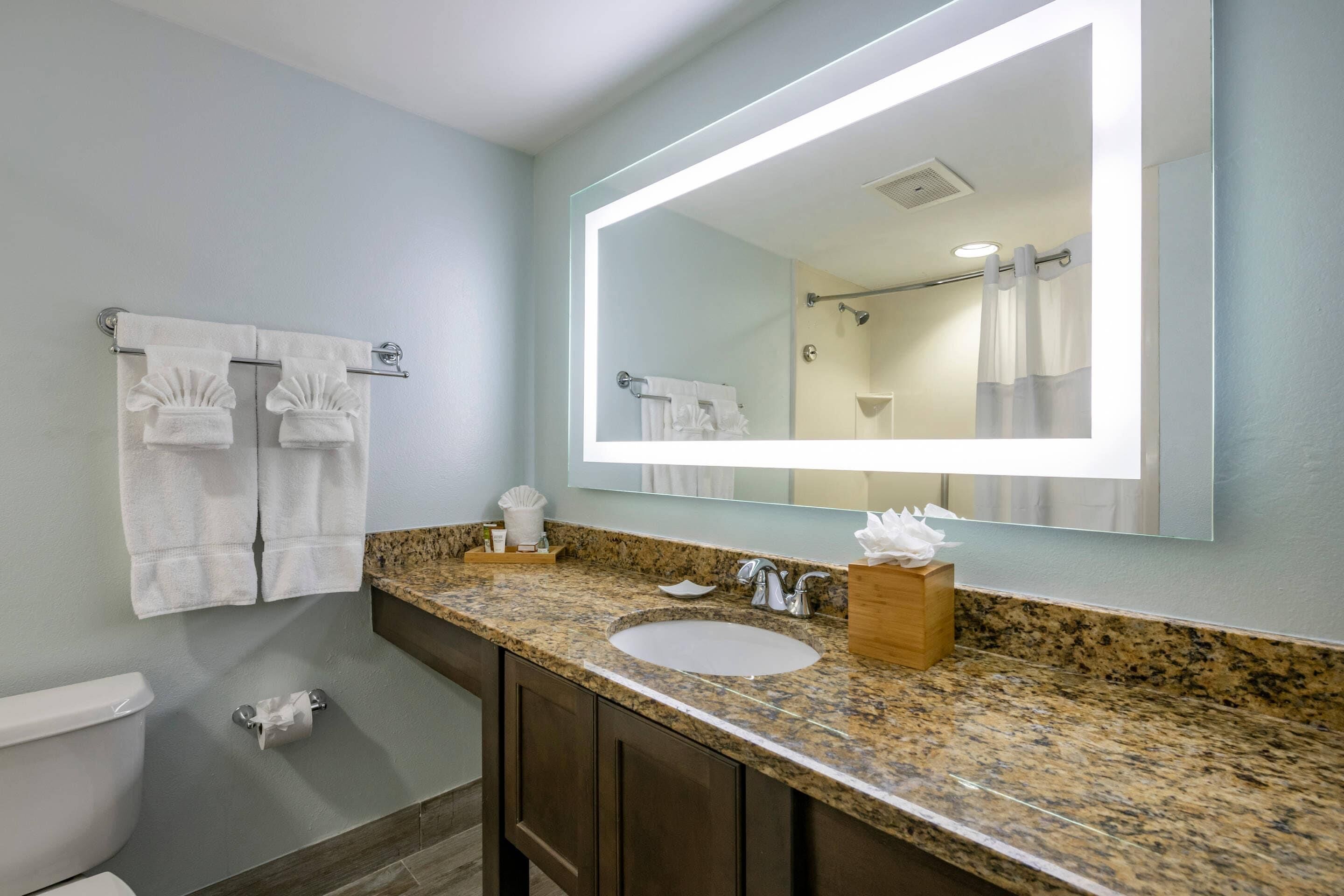 A bathroom with a granite countertop, a sink, a mirror, and a towel rack.