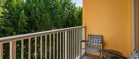 A balcony with a white railing, two wicker chairs, and a small table.