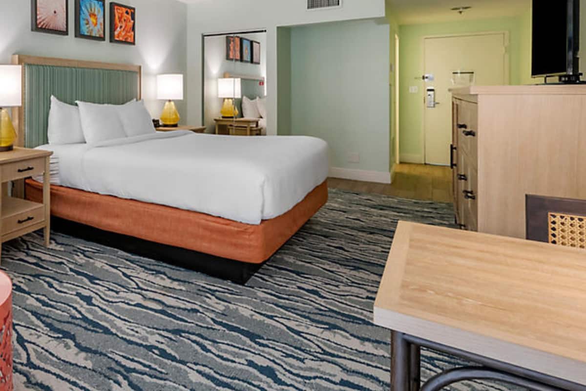 Una habitación de hotel con cama, mesitas de noche, lámparas, cómoda y televisor.