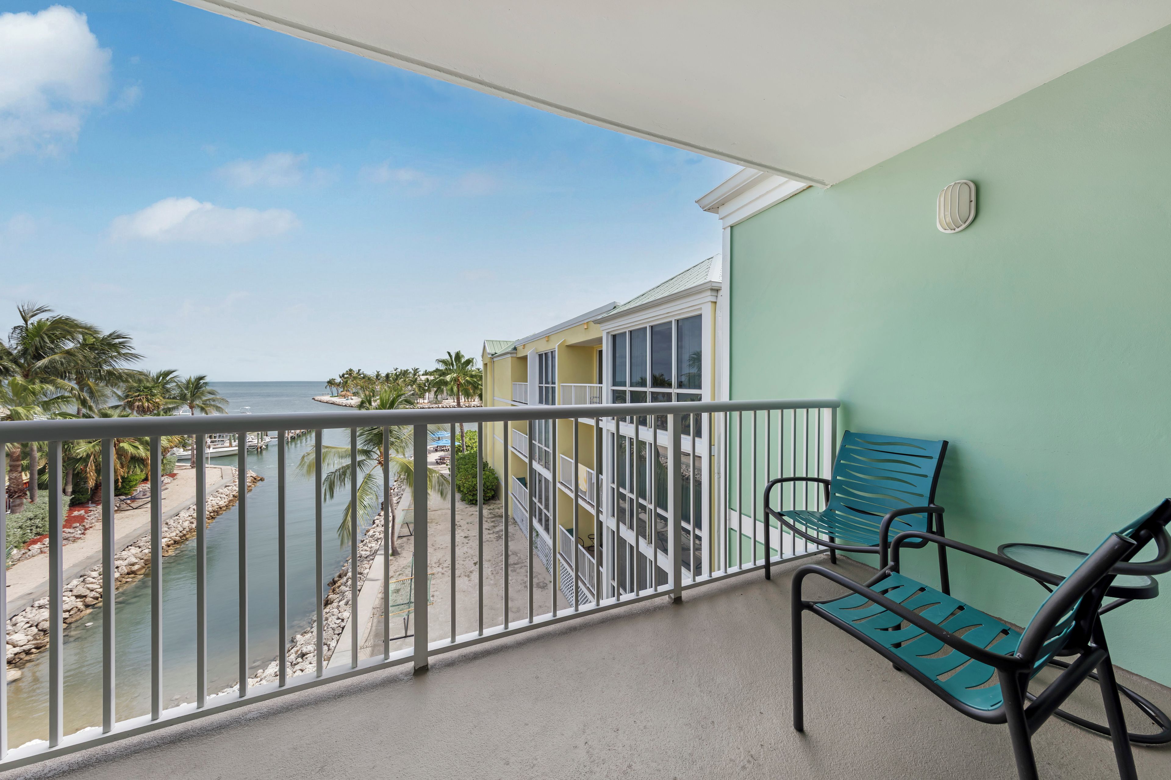 A balcony with a view of the sea, a chair, and a building with a green wall.