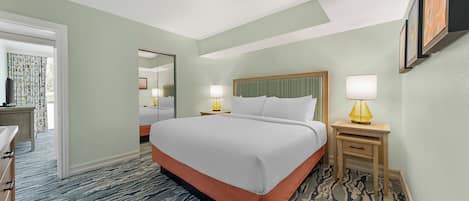 Une chambre d’hôtel avec un grand lit, deux tables de chevet avec des lampes, un miroir et une porte donnant sur une salle de bain.