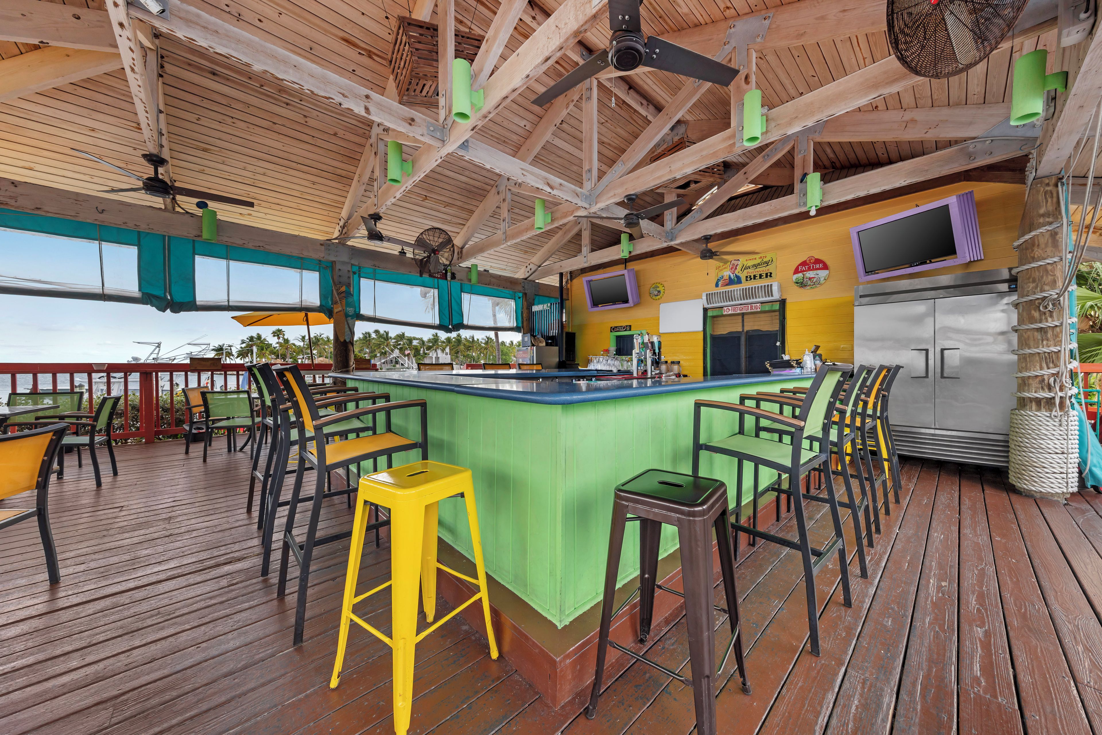 A bar area with a wooden deck, green bar stools, and a counter with a TV screen.