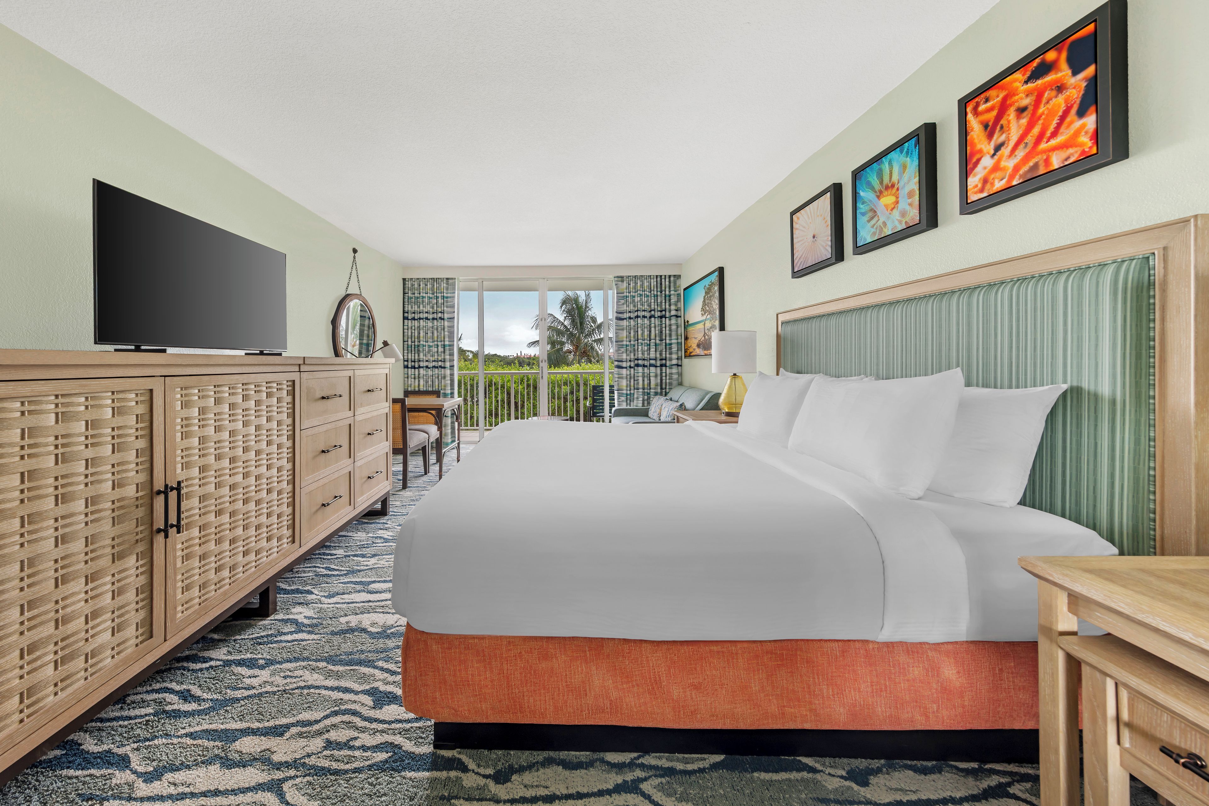 A hotel room with a large bed, a television, a wooden cabinet, and a view of the outdoors.