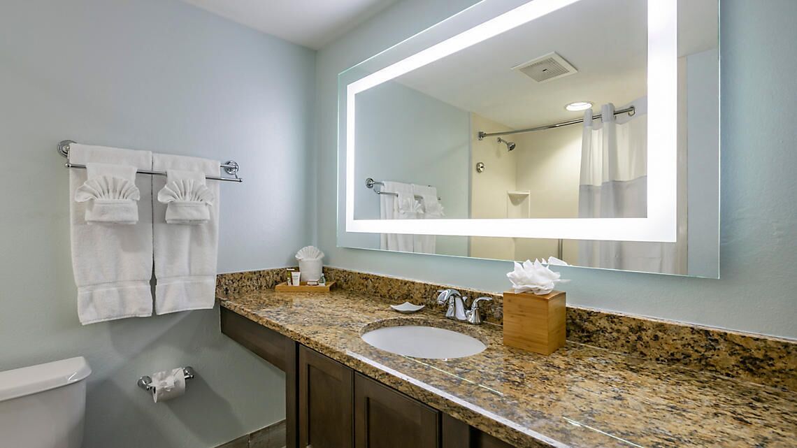 A bathroom with a granite countertop, a sink, a mirror, and two towels hanging on a rack.