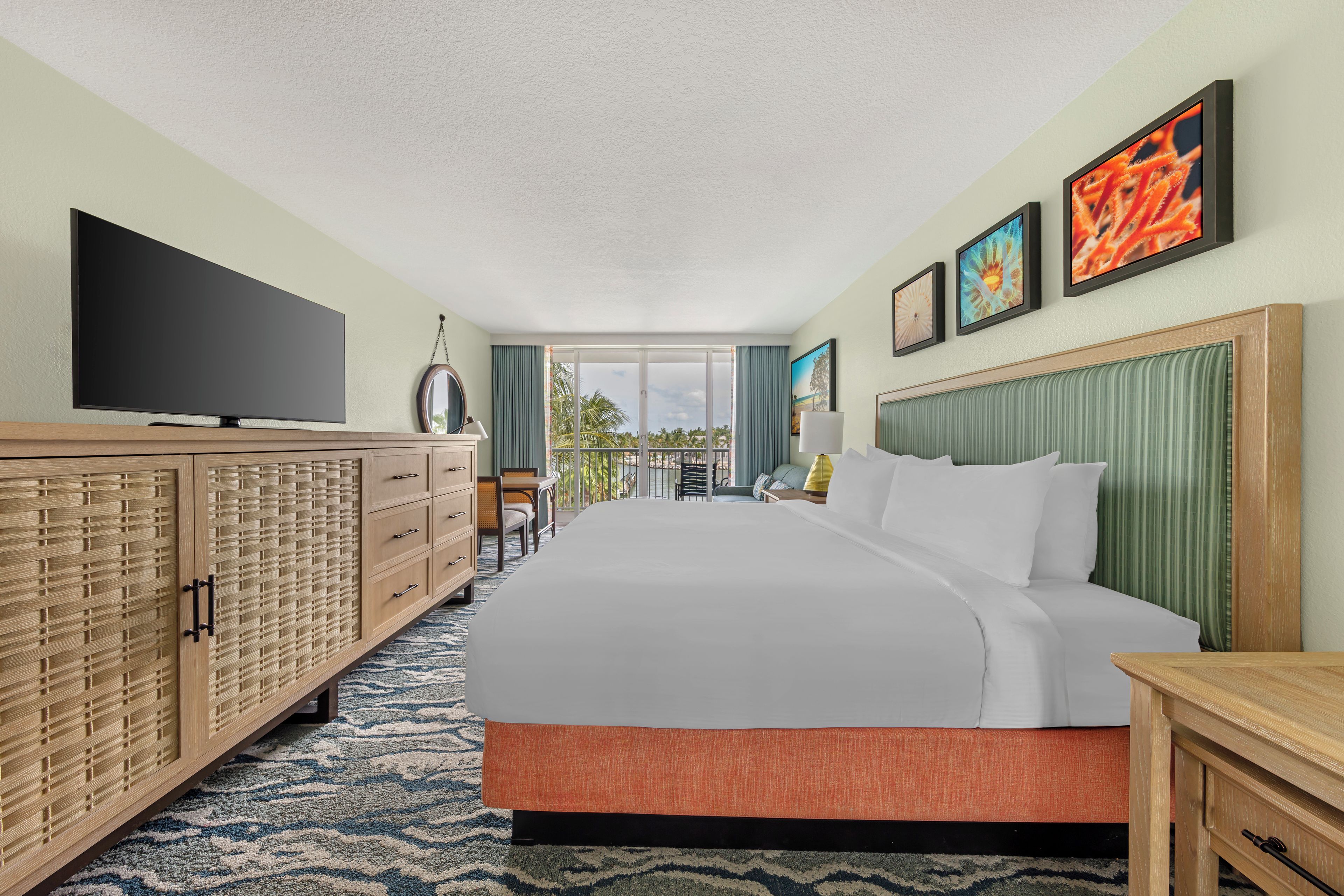 A hotel room with a large bed, a television, a wooden cabinet, and a view of the outdoors.