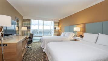 A hotel room with two beds, a desk, a chair, and a large window with curtains.