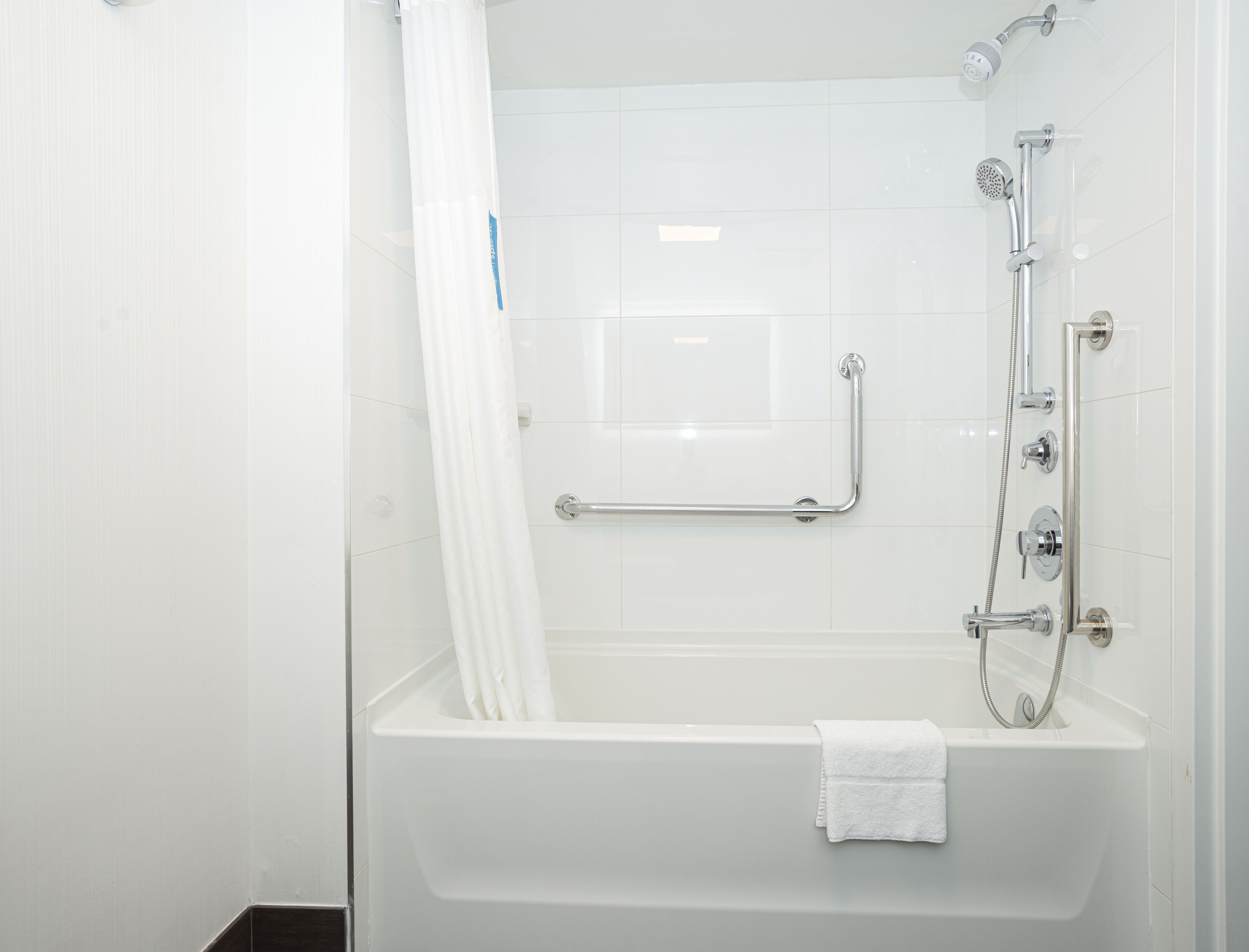 Ein modernes Badezimmer mit Badewanne, Dusche und Haltegriffen.