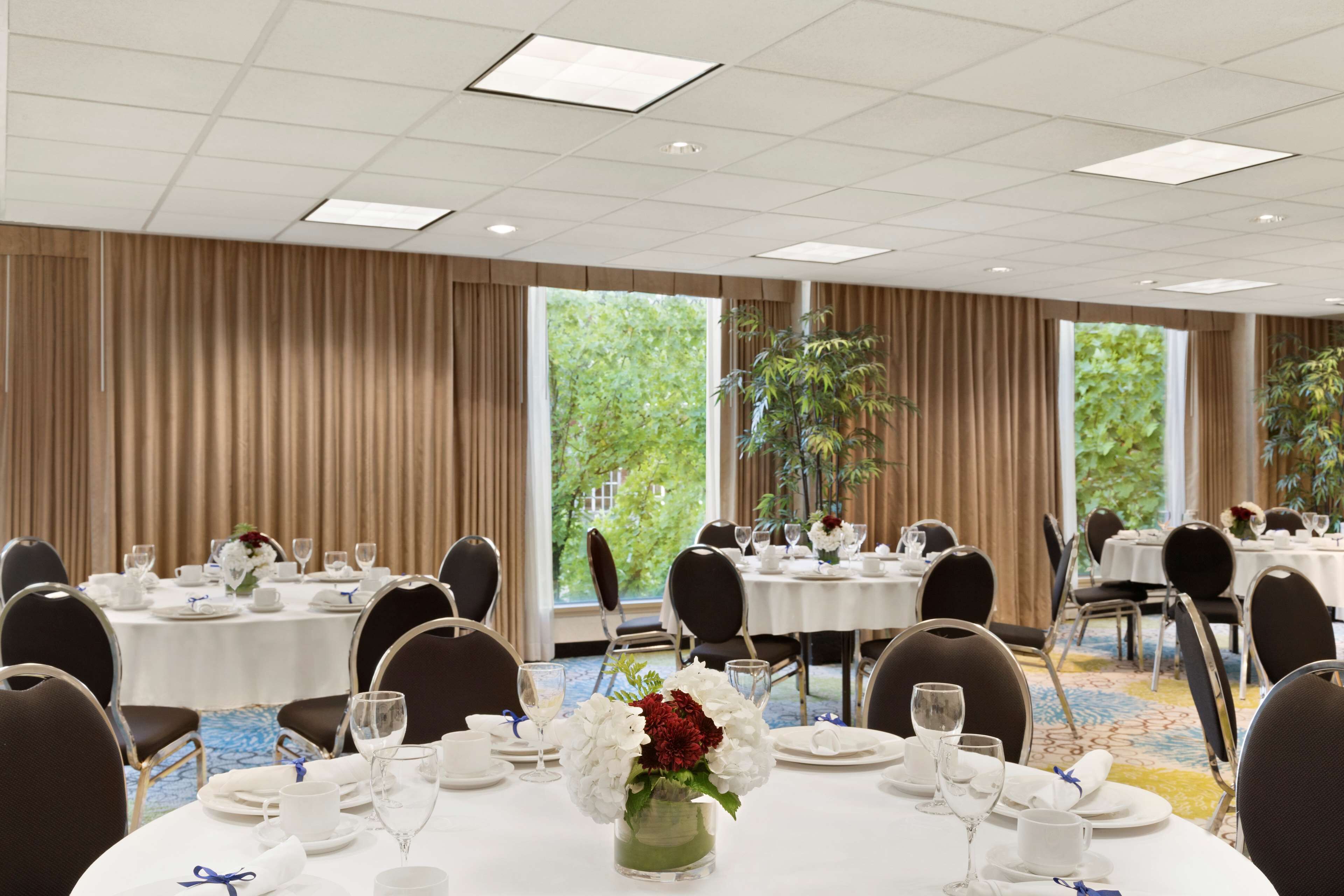 A conference room with round tables, chairs, and a large window with a view of greenery.