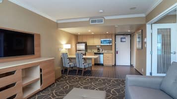 Hotelkamer met flatscreen televisie, een bank, een eethoek met gestreepte stoelen, een keuken met magnetron en een kamerbreed tapijt met patroon.