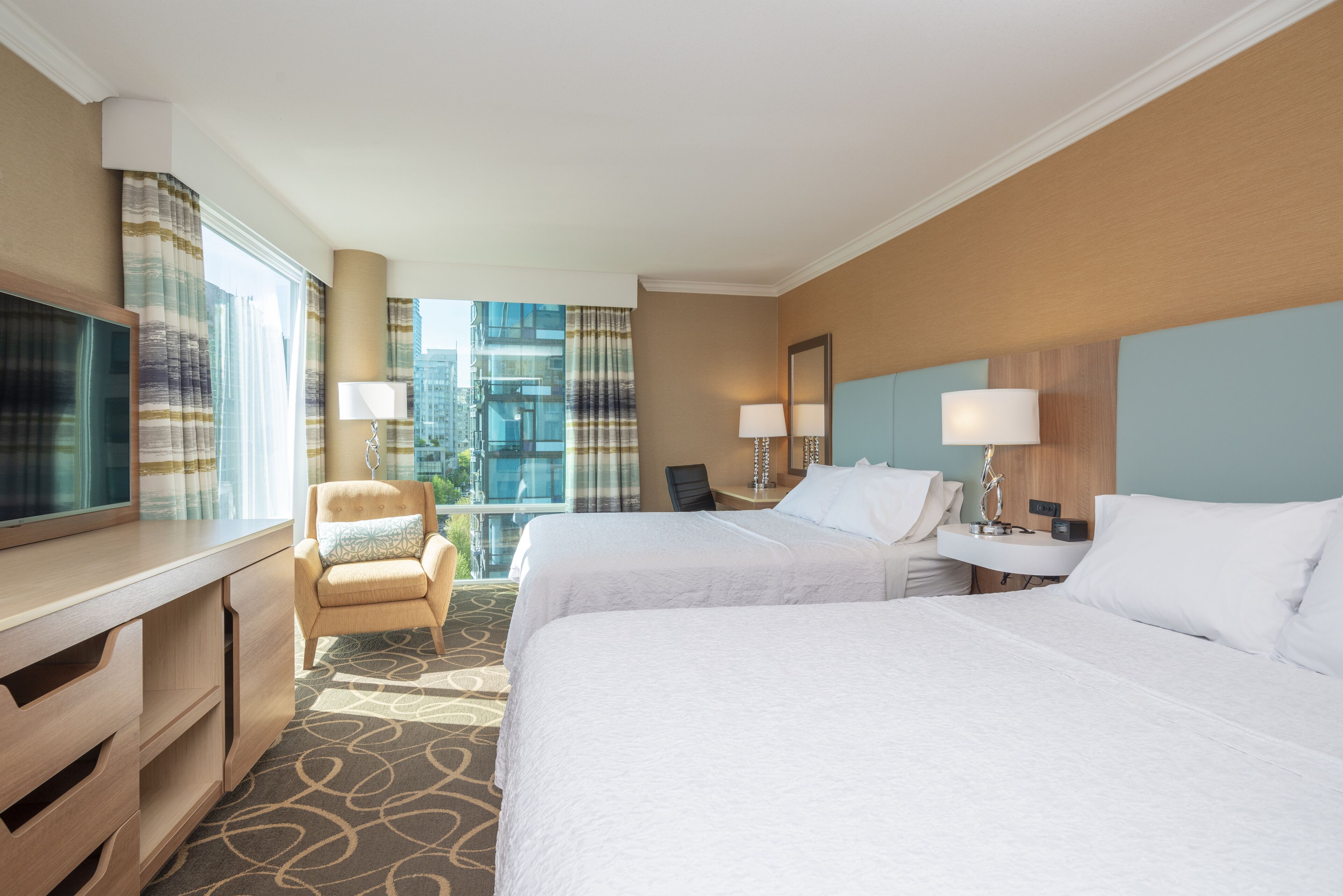 A hotel room with two beds, a desk, a chair, and a TV.