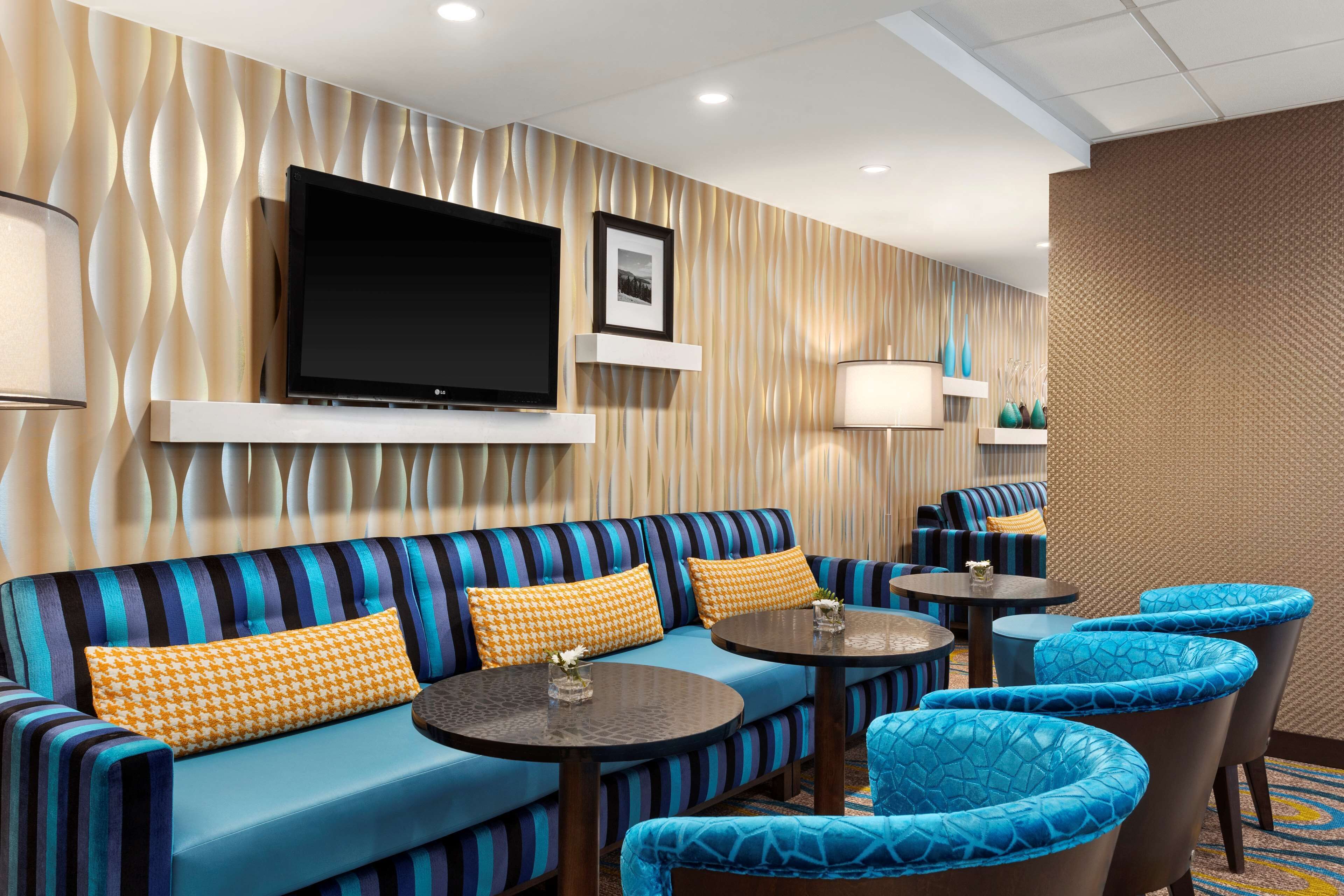 A hotel lobby with a striped sofa, round tables, and blue cushioned chairs.