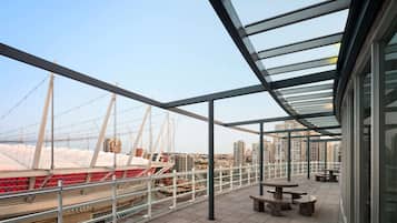 A rooftop terrace with a glass balustrade, seating area, and a view of the harbor with boats and buildings.