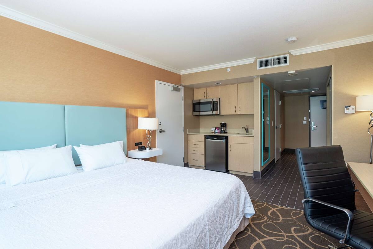 Habitación de hotel con cama, escritorio, silla, microondas, cafetera y kitchenette.