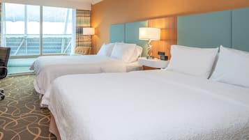 A hotel room with two beds, a large window, a chair, and a desk with a lamp.