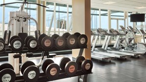 Ein Fitnessstudio mit Gewichthebern, Laufbändern und einem großen Fenster mit Blick auf Gebäude.