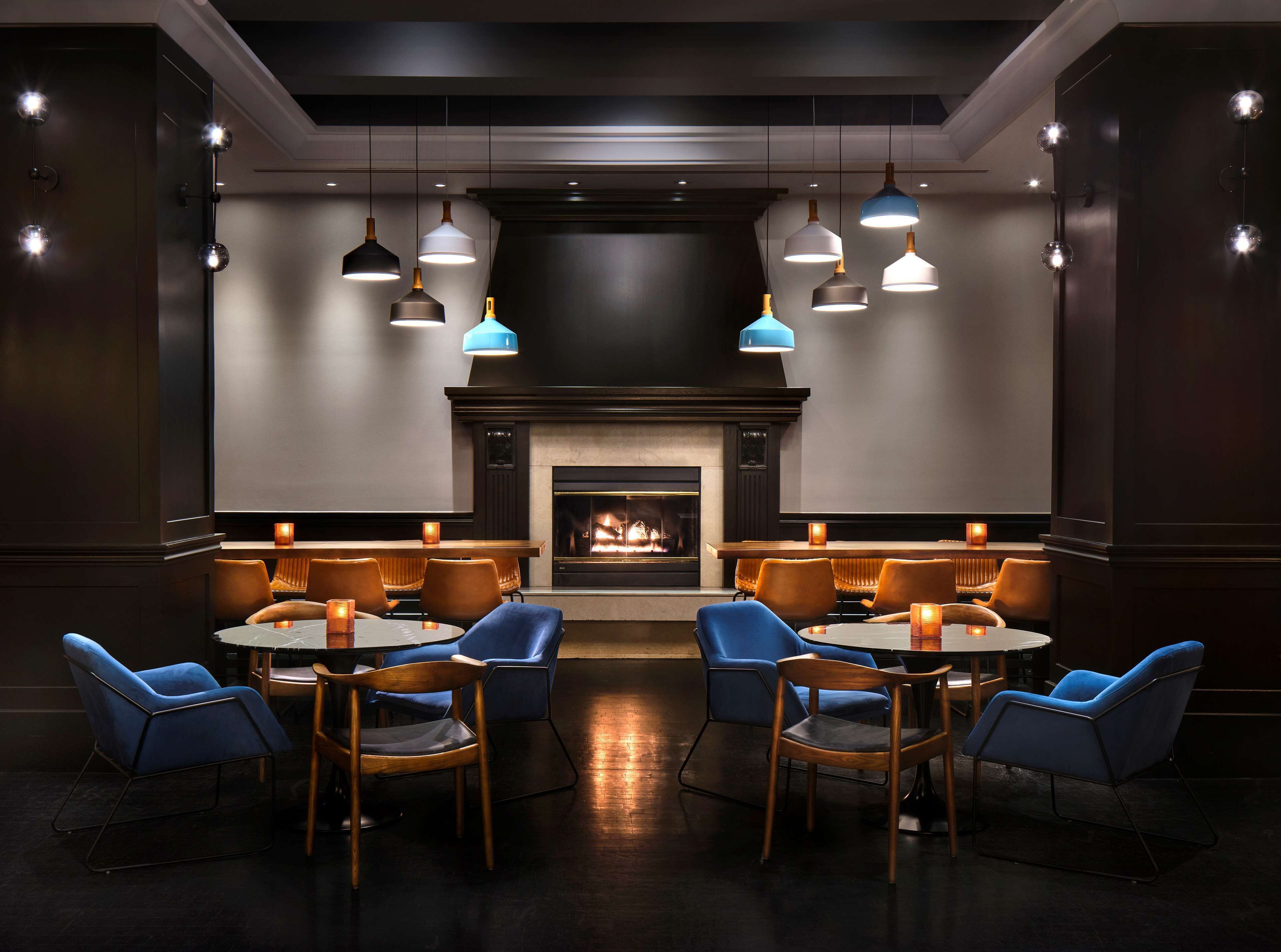 Een moderne lounge met een open haard, ronde tafels en blauwe stoelen.