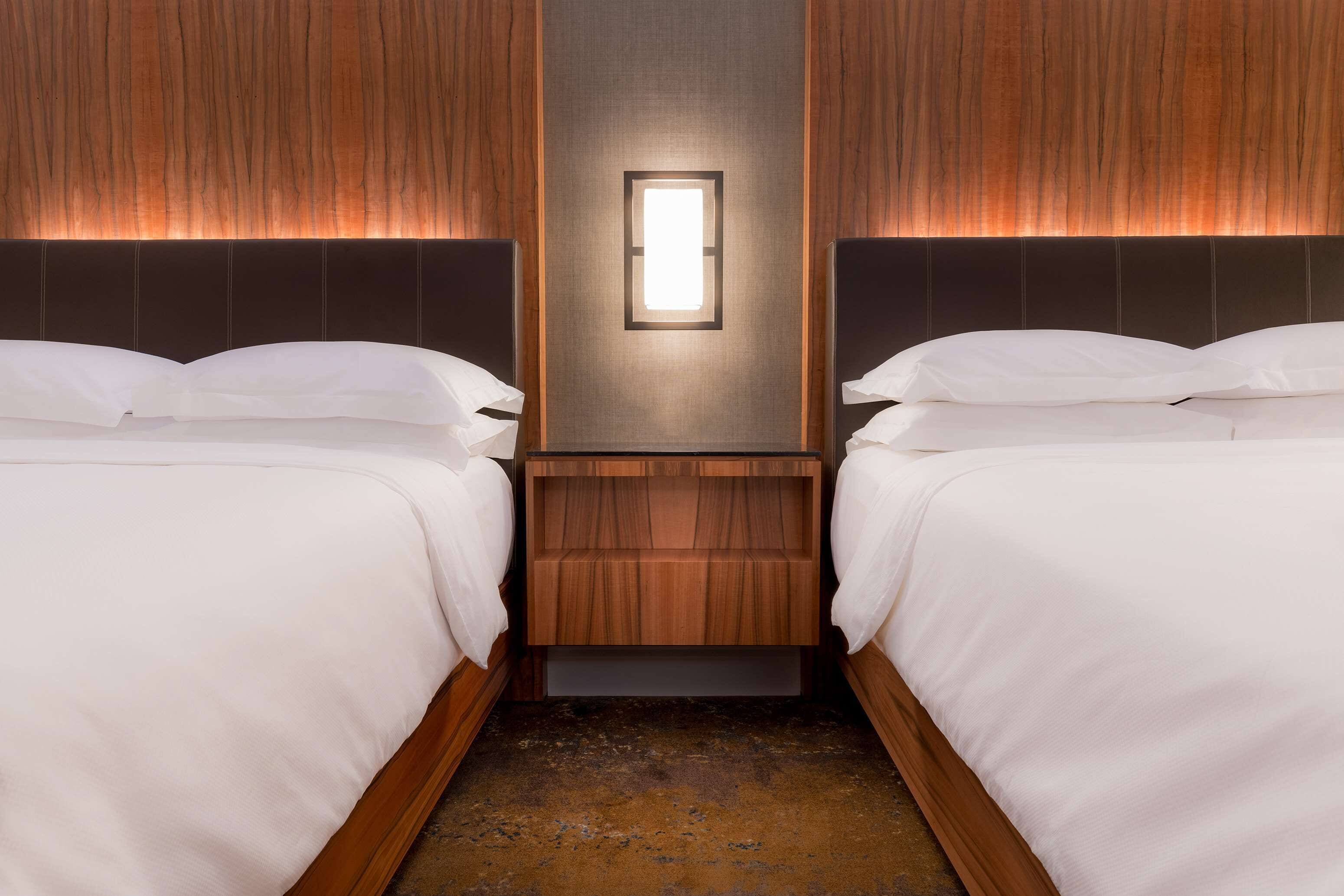 A hotel room with two beds, a central light fixture, and wooden paneling on the walls.