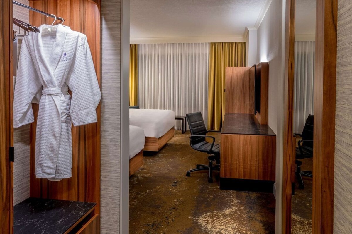 A hotel room with a wooden wardrobe, a bed, a desk, and a mirror.
