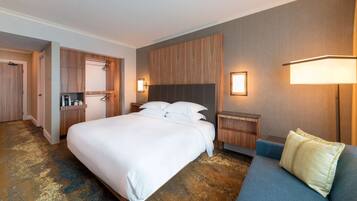 Une chambre d’hôtel avec un grand lit, un canapé, une tête de lit en bois et une armoire.