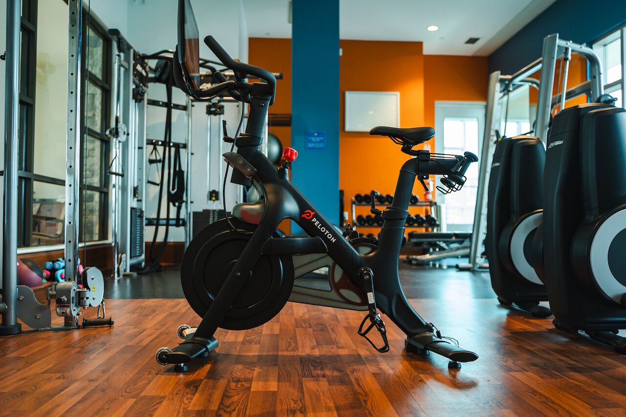 Un vélo d’appartement, des appareils de musculation et un miroir dans une salle de sport dotée d’un plancher en bois et de murs orange.