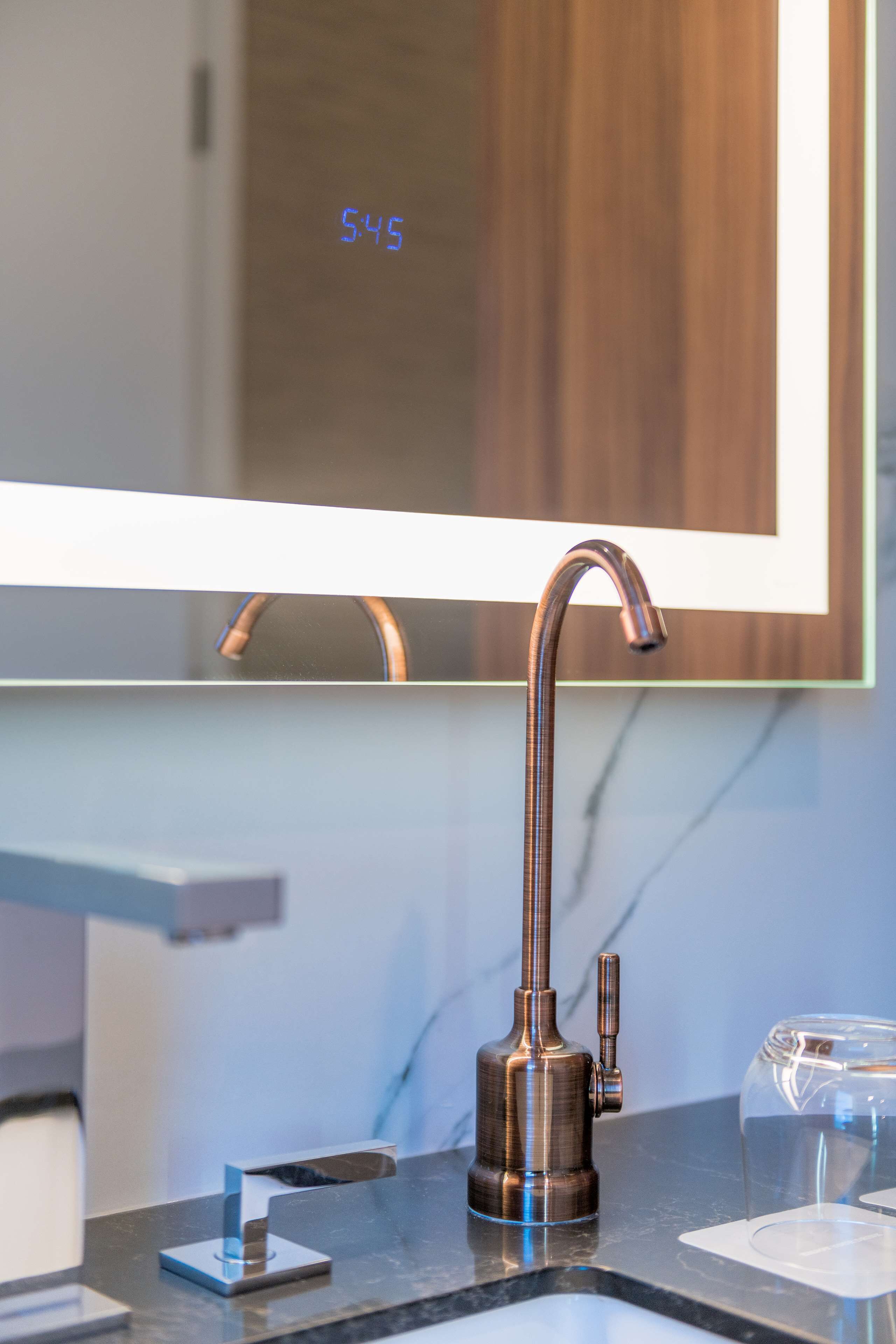 Un baño con un grifo moderno, un espejo y un recipiente de vidrio sobre el mostrador.