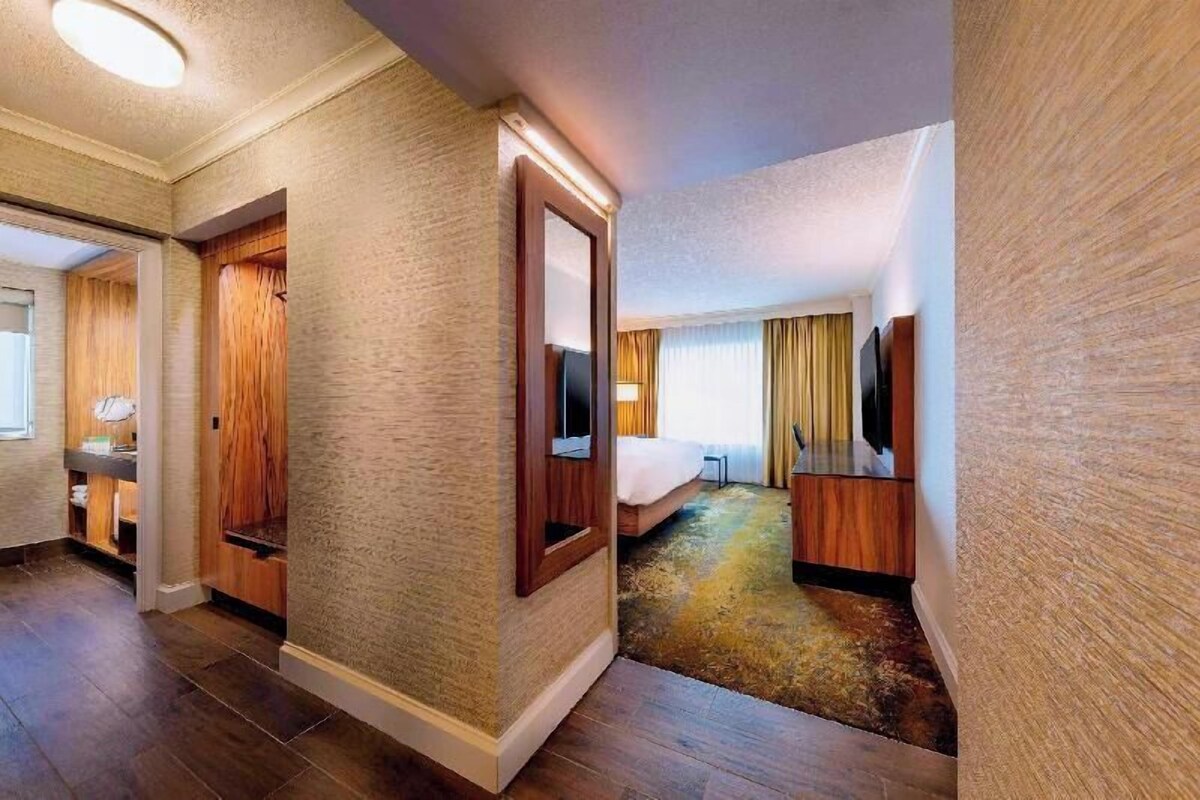 A hotel room with a bed, a TV, a desk, and a mirror.