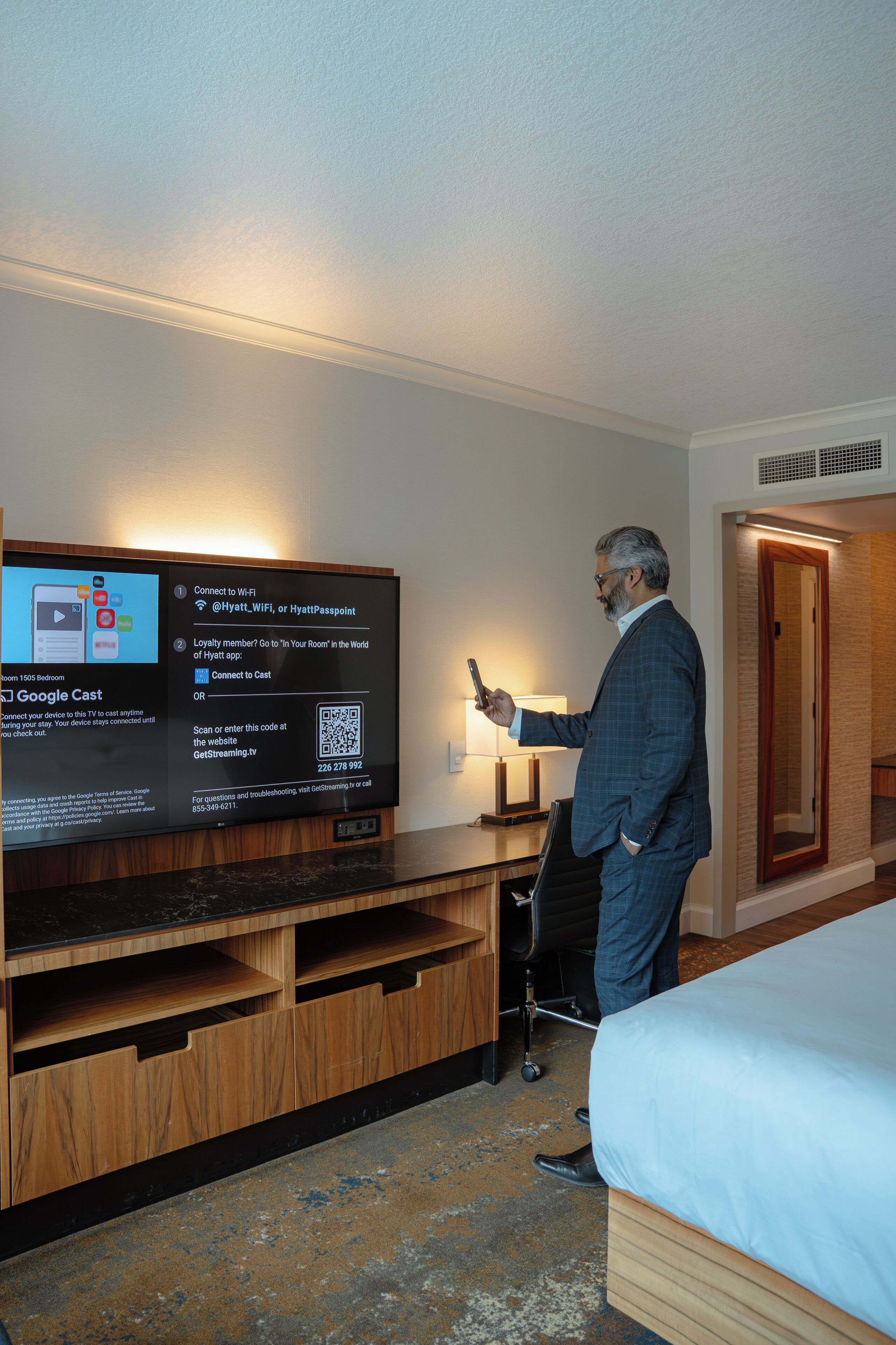 Une chambre d’hôtel équipée d’une télévision affichant une application hôtelière, d’un lit, d’un bureau avec une lampe et d’une porte.