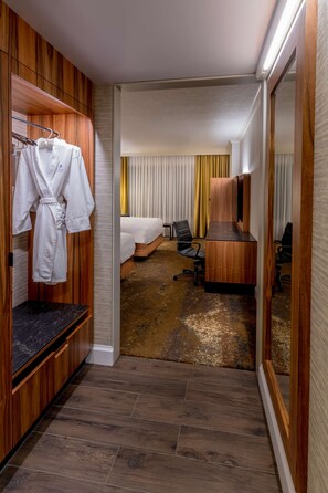 A hotel room with a wooden wardrobe, a desk, a bed, and a seating area.