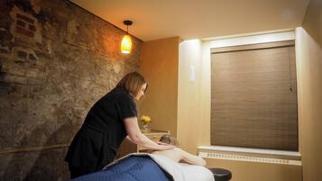 A massage therapy room with a brick wall, a wooden cabinet, and a window with blinds.