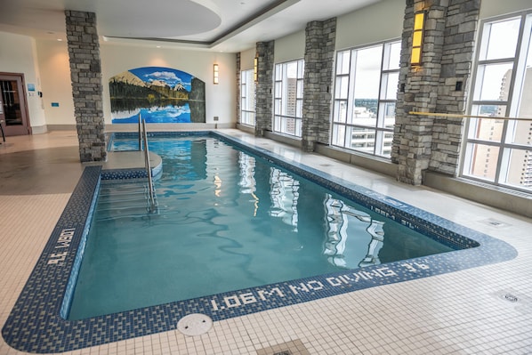 An indoor swimming pool with clear water, stone pillars, and a mural of a mountain landscape.