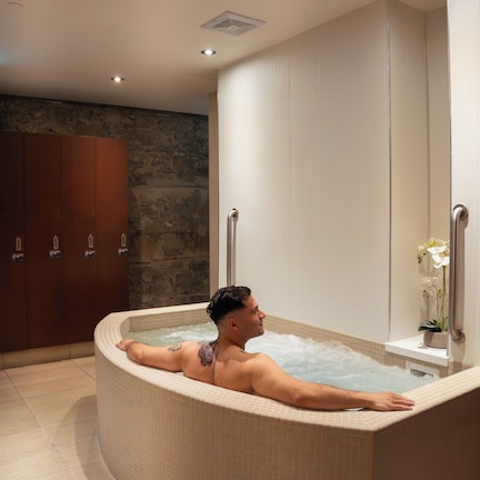 A person relaxing in a hot tub with a stone wall and wooden cabinets in the background.