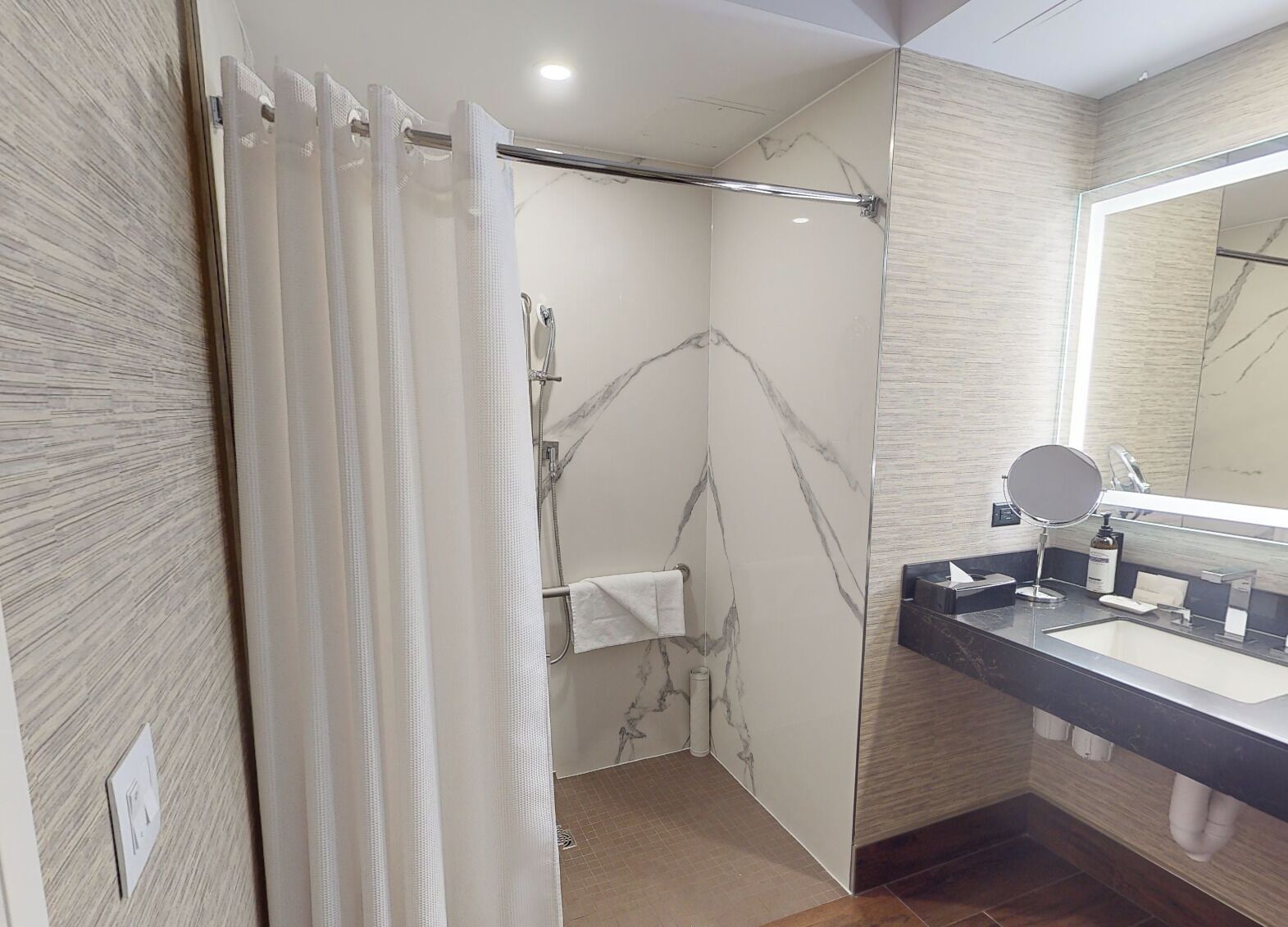 Un baño moderno con ducha, tocador con espejo y paredes con diseño de mármol.
