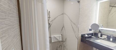 Un baño moderno con ducha, tocador con espejo y paredes con diseño de mármol.