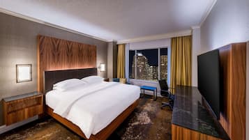 A hotel room with a large bed, a desk, a TV, and a city view.