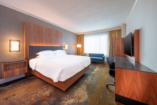 Una habitación de hotel con una cama grande, un escritorio con televisor de pantalla plana, una silla y un sofá.