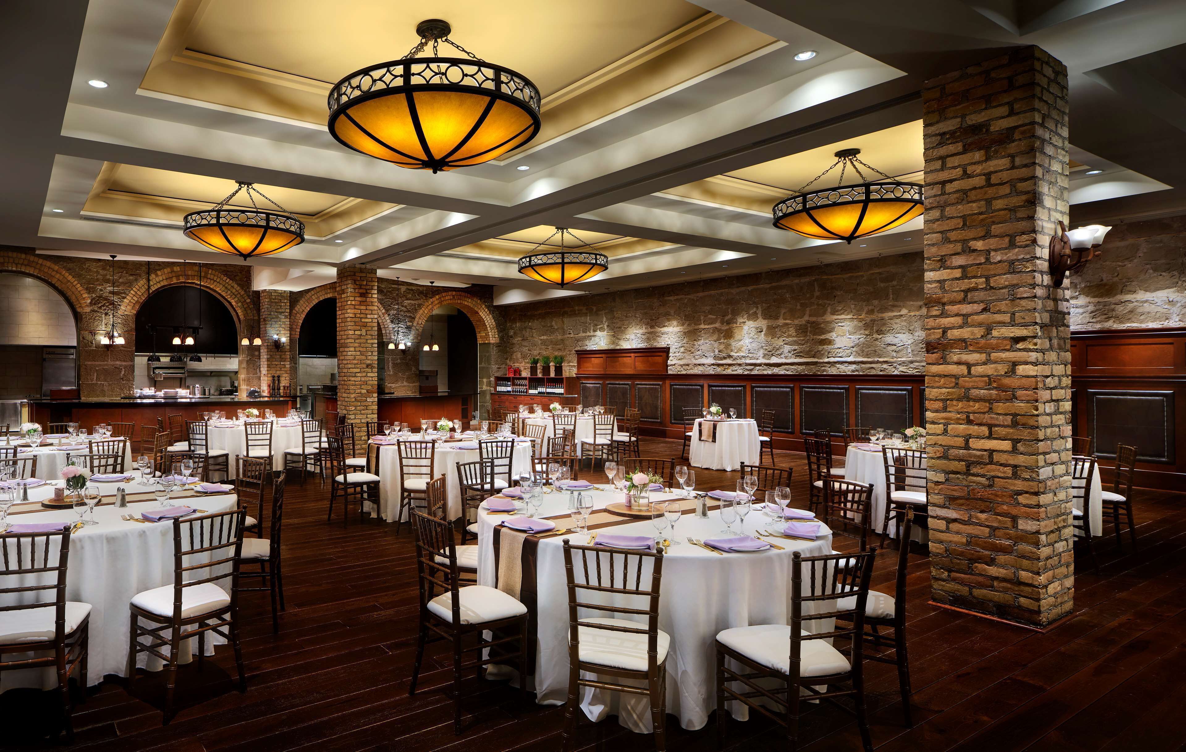 Un salón de banquetes con mesas redondas, manteles blancos y sillas de madera.