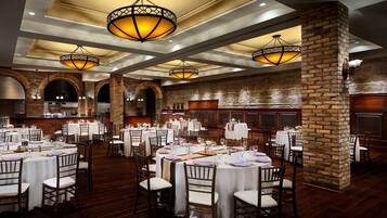 Un salón de banquetes con mesas redondas, manteles blancos y sillas de madera.