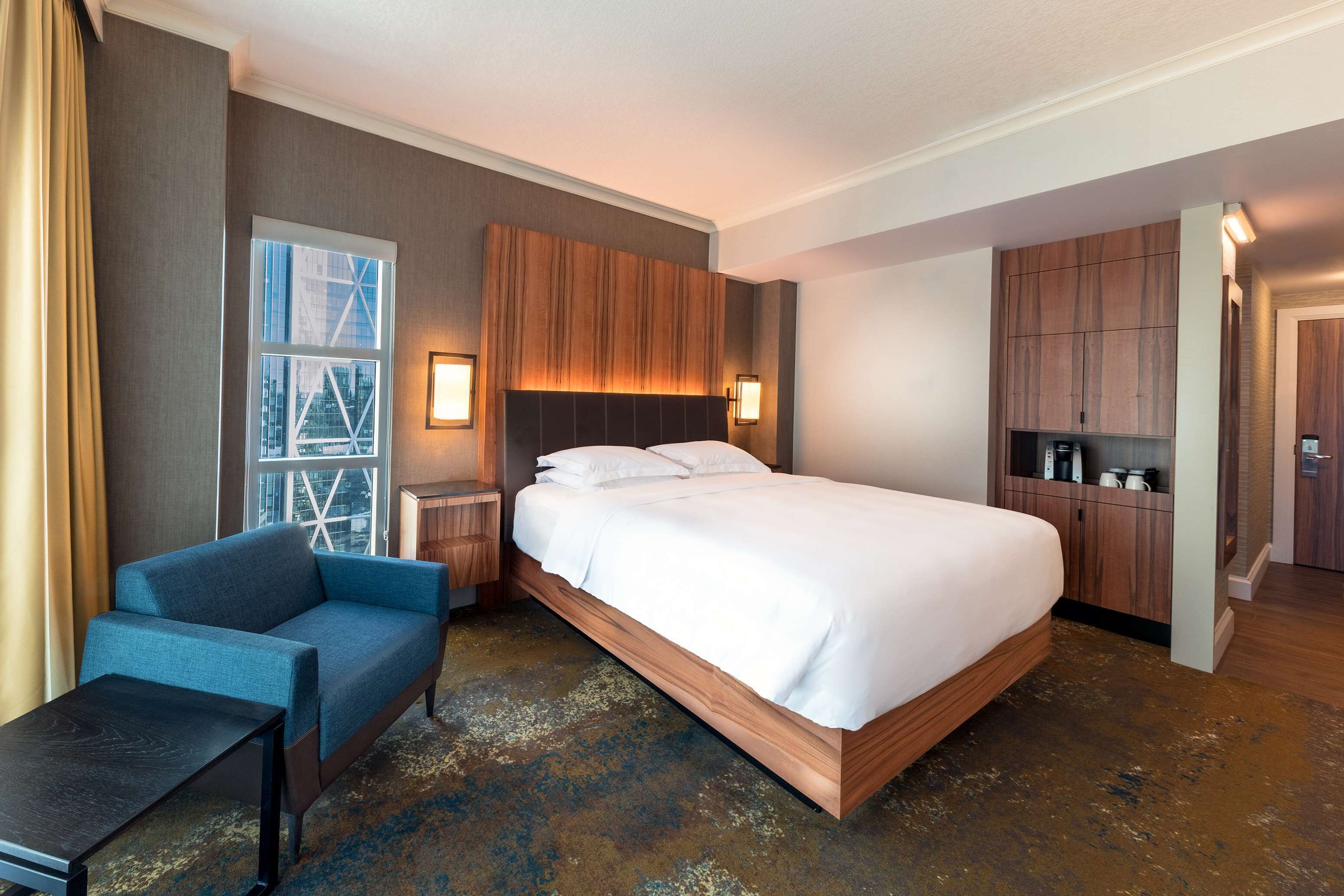 A hotel room with a large bed, a blue sofa, a small table, and a wardrobe.