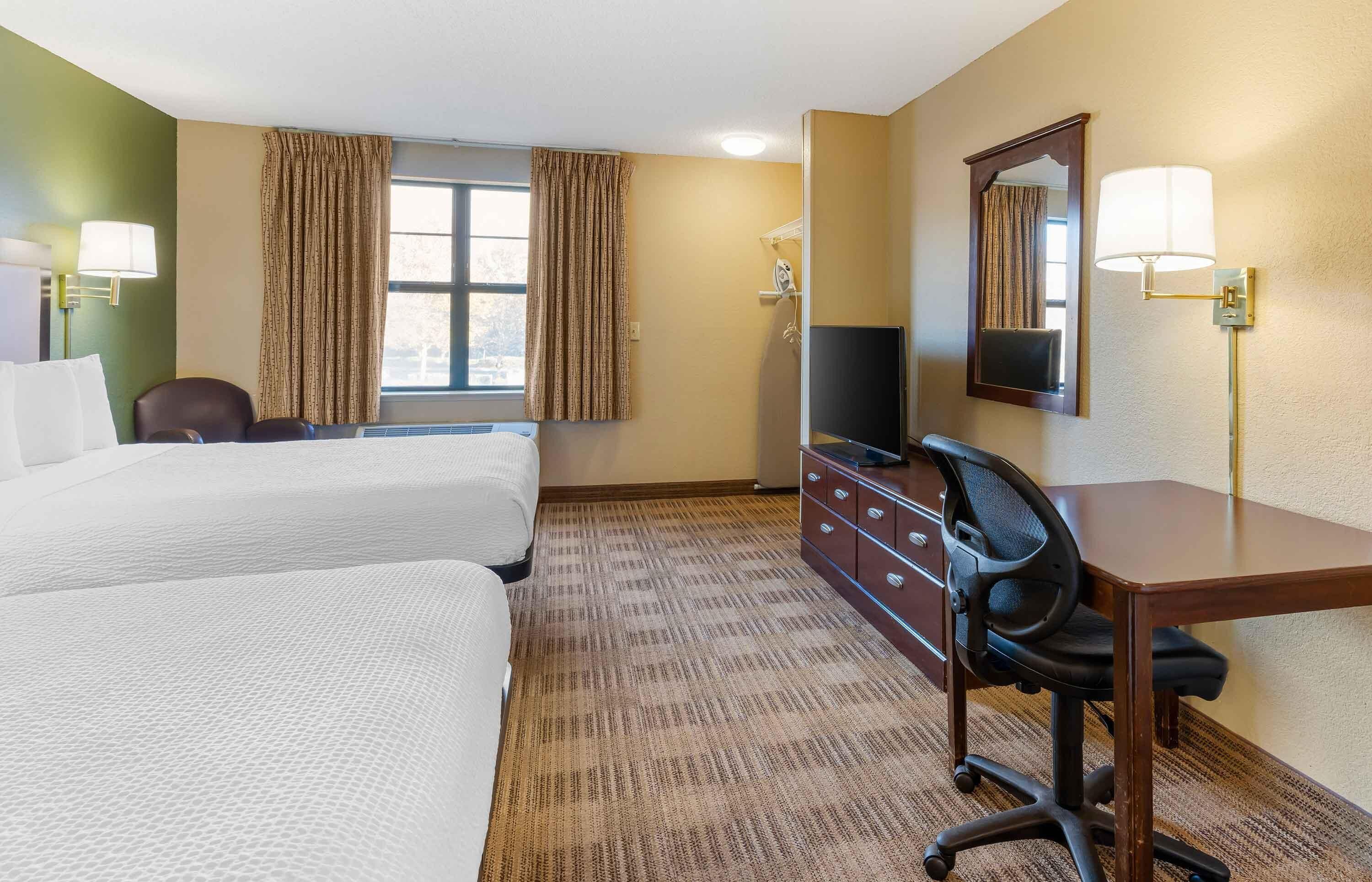 A hotel room with two beds, a desk, a chair, a television, and a mirror.