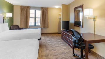 A hotel room with two beds, a desk, a chair, a television, and a mirror.