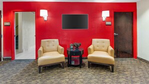 A hotel lobby with a red wall, two leather armchairs, a small round table with a decorative item, and a blackboard.