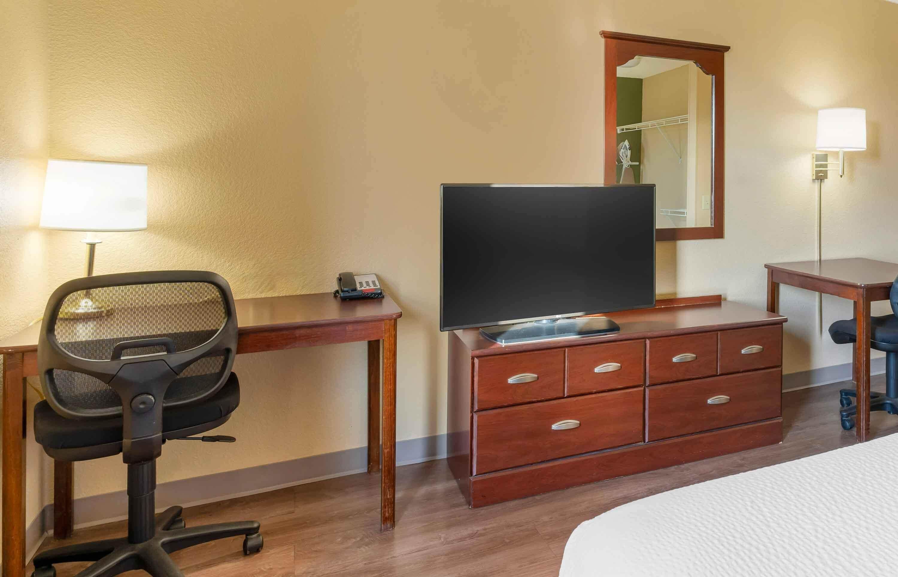 Habitación de hotel con escritorio, silla, televisor, cómoda y espejo.