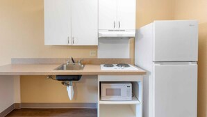 A small kitchen with white cabinets, a sink, a stove, a microwave, and a refrigerator.